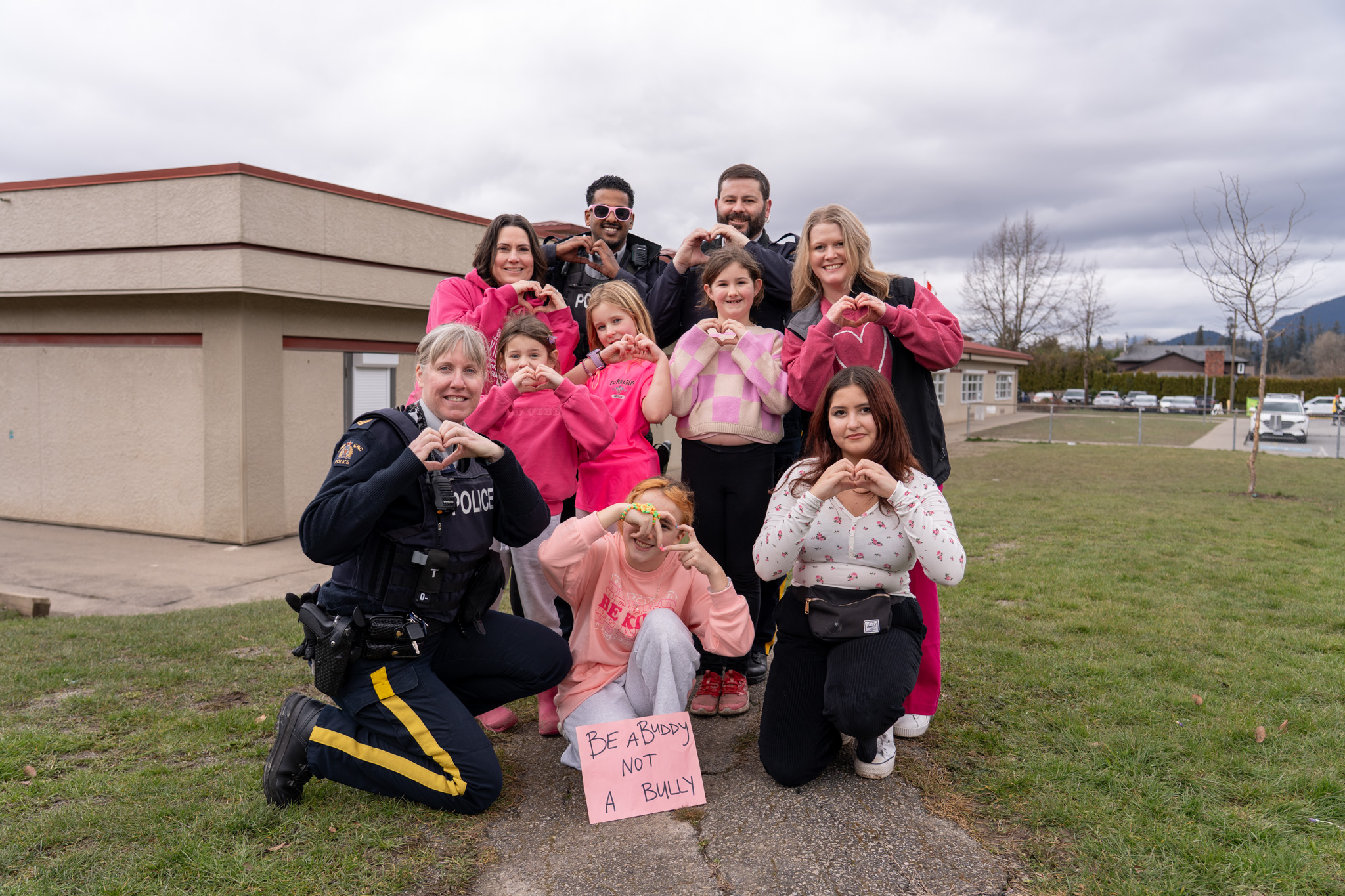 Alouette Elementary students, staff, and local RCMP staff make hearts with their hands as they pose for a photo outside of the school.
