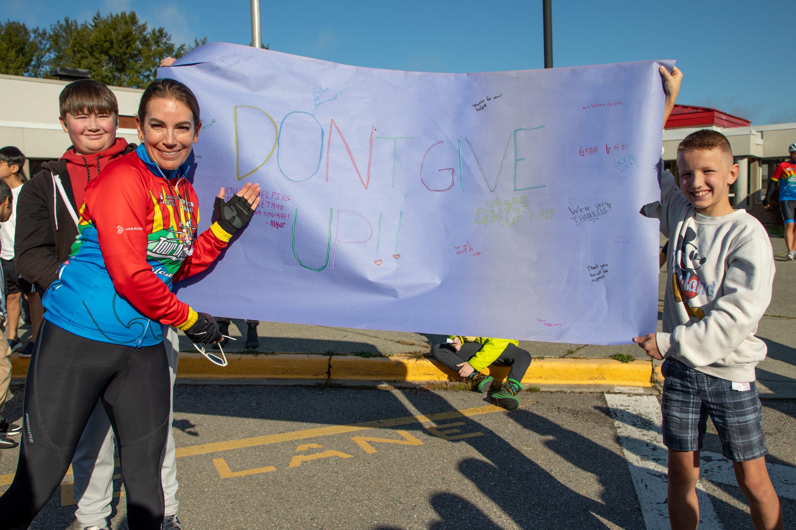 Albion Cops for Cancer-03 Cyclist poses with sign that reads, "Don't give up!"