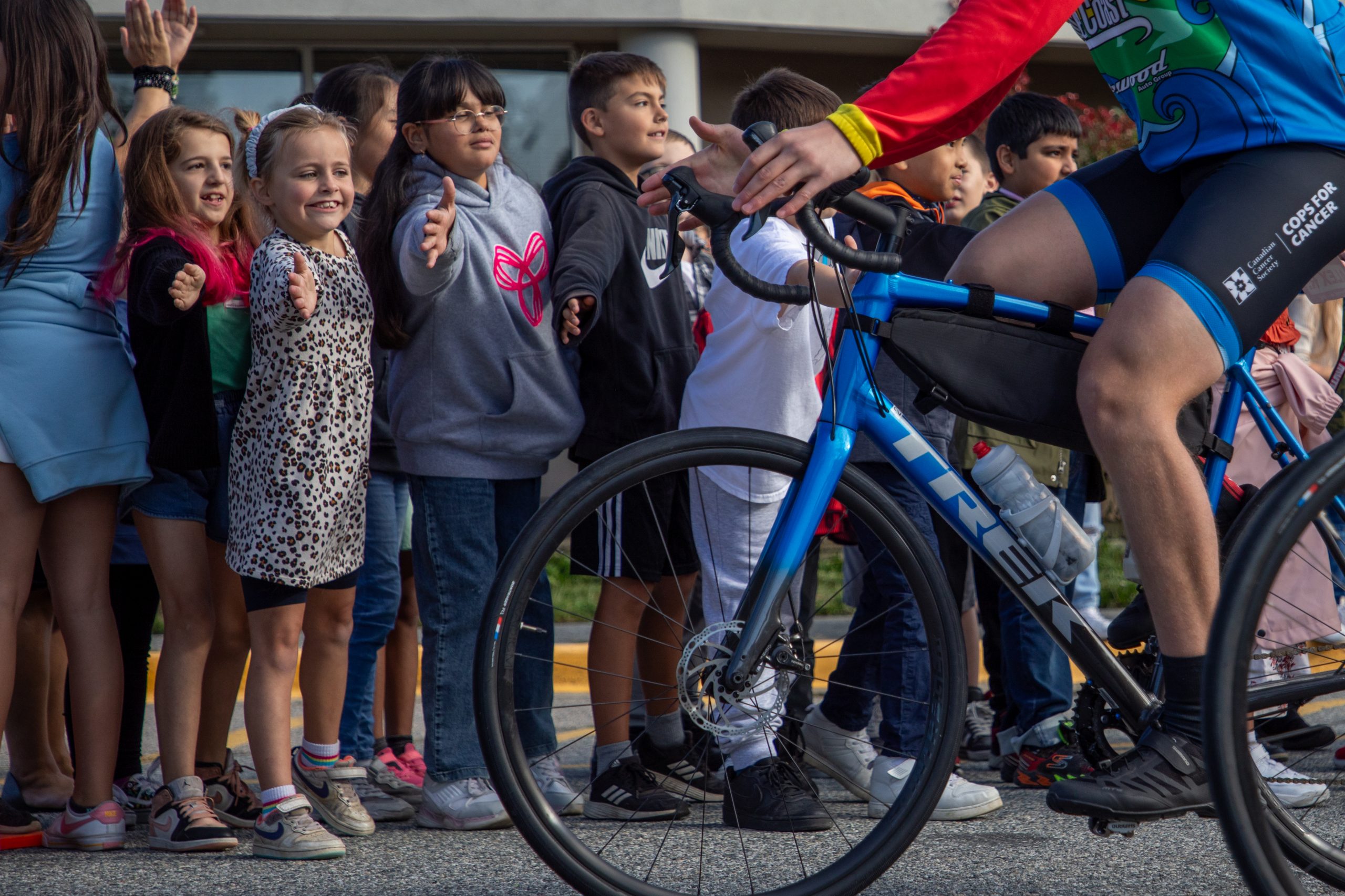 Cyclist from Cops for Cancer Tour de Coast are greeted by excited students holding their hands out.