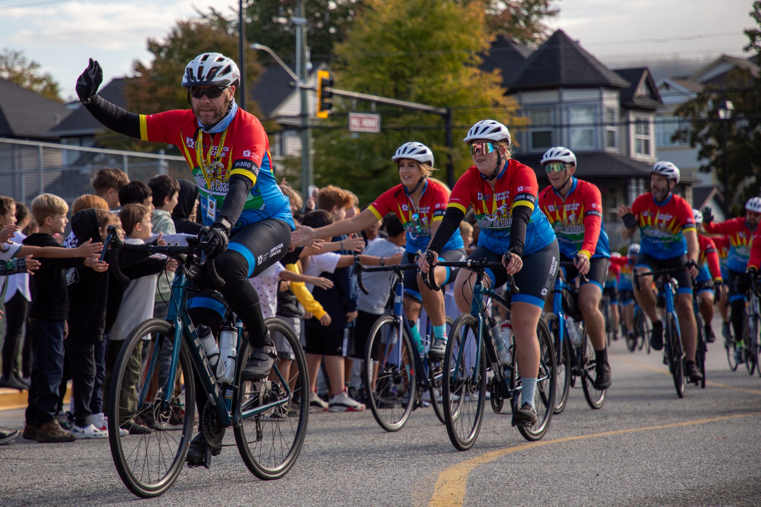 Albion Cops for Cancer-18 Cyclists from Cops for Cancer Tour de Coast are greeted by excited students holding their hands out.