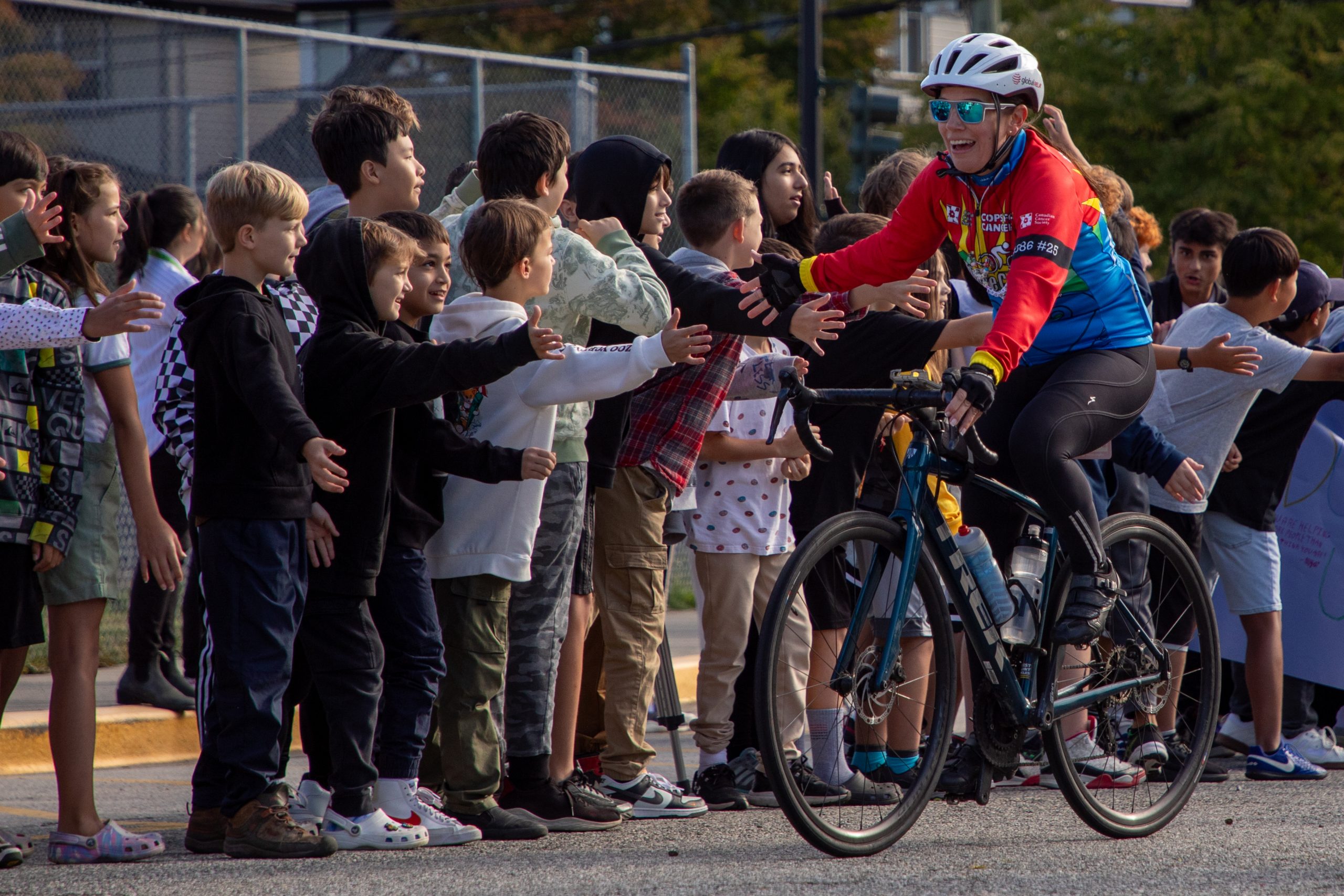 Albion Cops for Cancer-20 Cyclist from Cops for Cancer Tour de Coast are greeted by excited students holding their hands out.