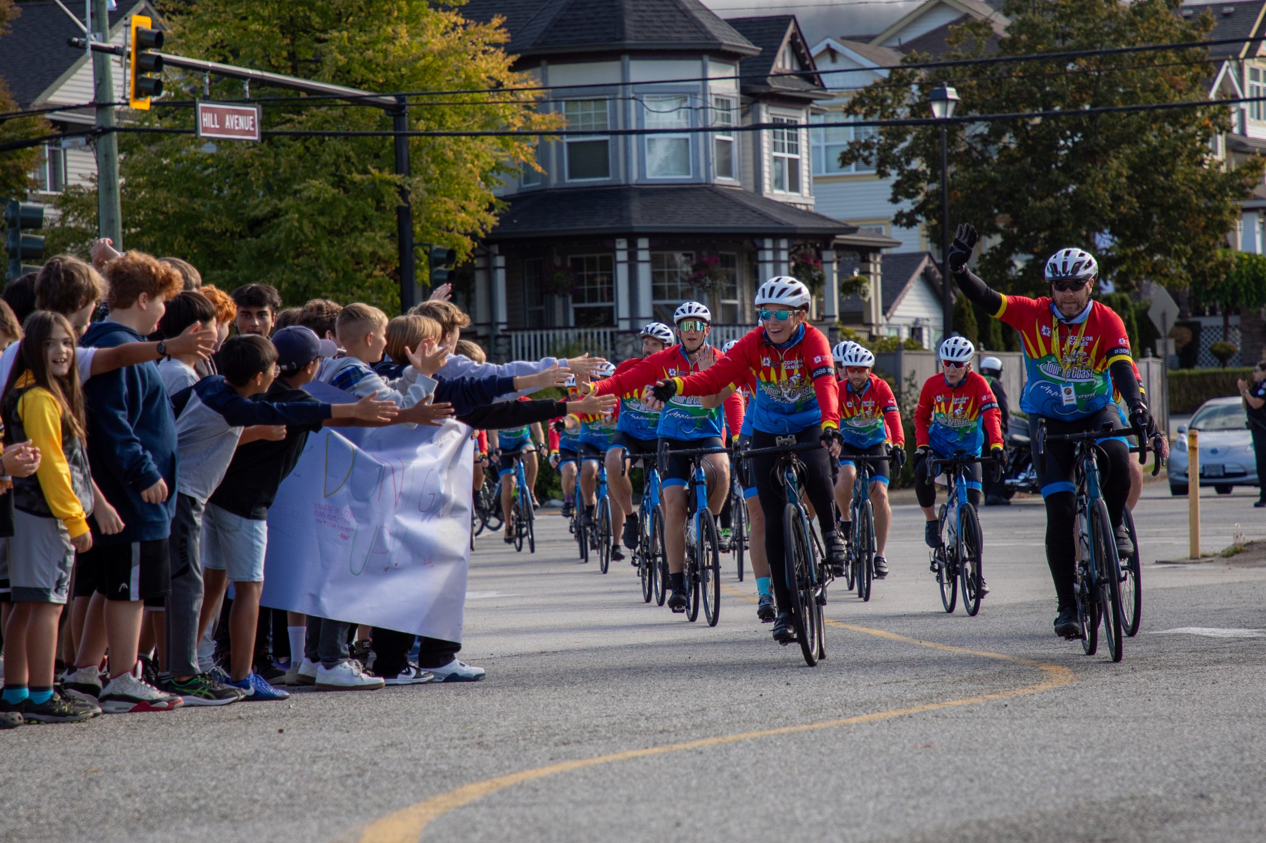 Albion Cops for Cancer-21 Cyclists from Cops for Cancer Tour de Coast are greeted by excited students holding their hands out.