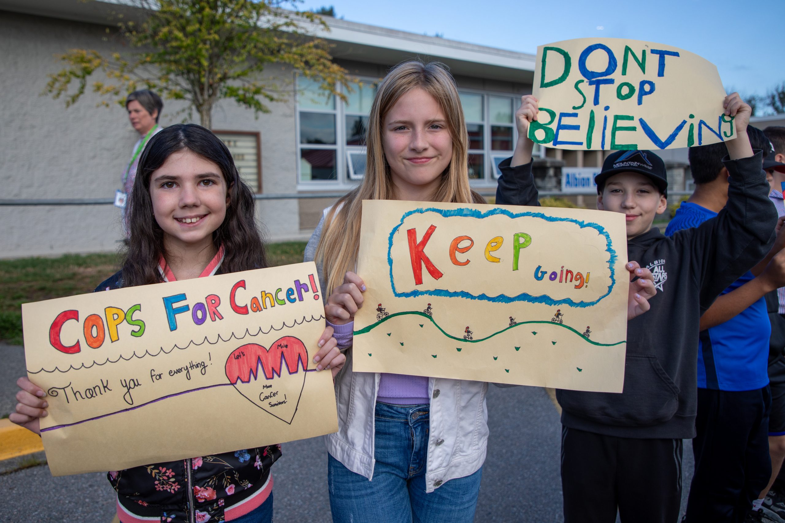 Students hold up signs at Albion Elementary cheering on the Cops for Cancer Tour de Coast.