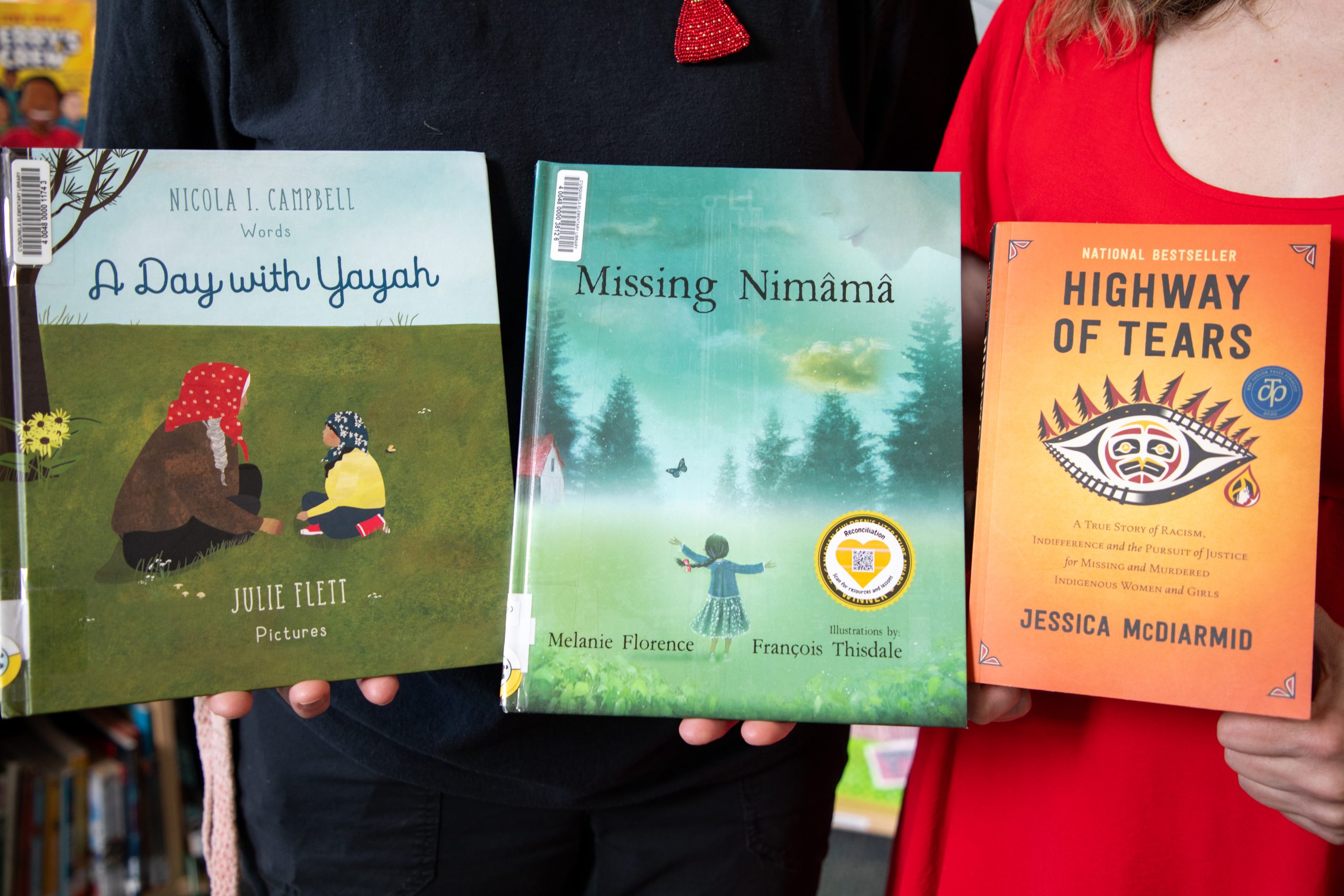 SD42 Aboriginal support worker Melinda Mouland and c̓əsqənelə Elementary teacher-librarian Janet Smith hold up "A Day with Yayah" by Nicola I. Campbell, "Missing Nimama" by Melanie Florence, and "Highway of Tears" by Jessica McDiarmid.
