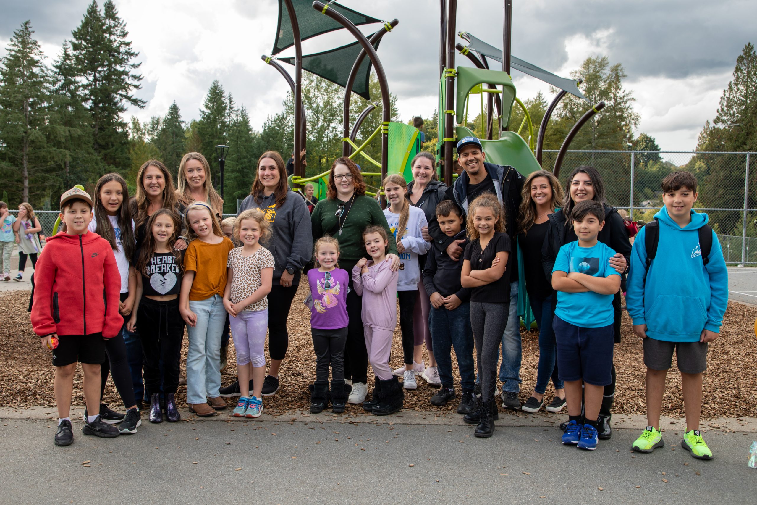 Members of c̓əsqənelə Elementary's PAC stand in front of the new playground with their children.