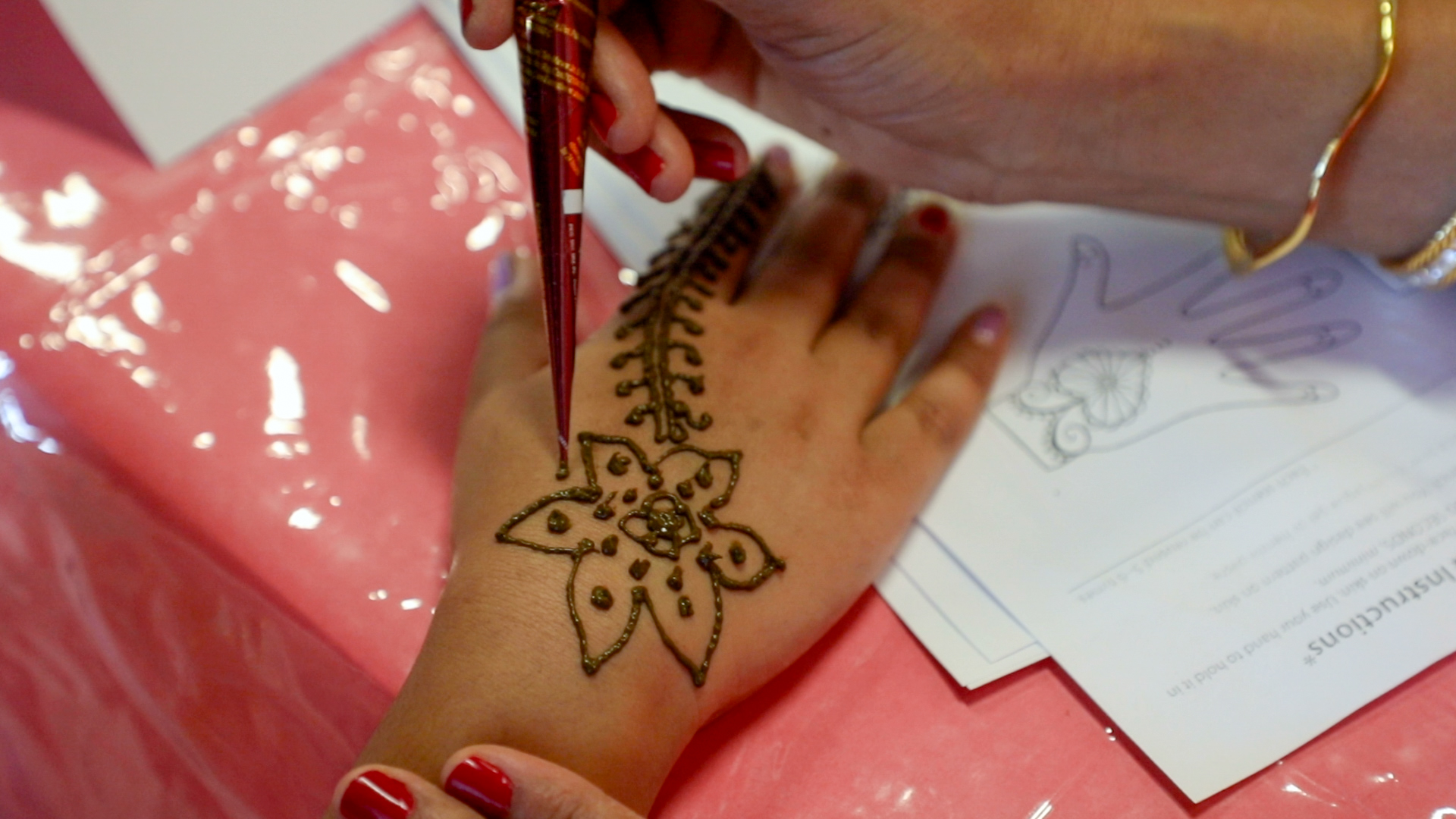 A flower design being painted onto a student's hand with mehndi.