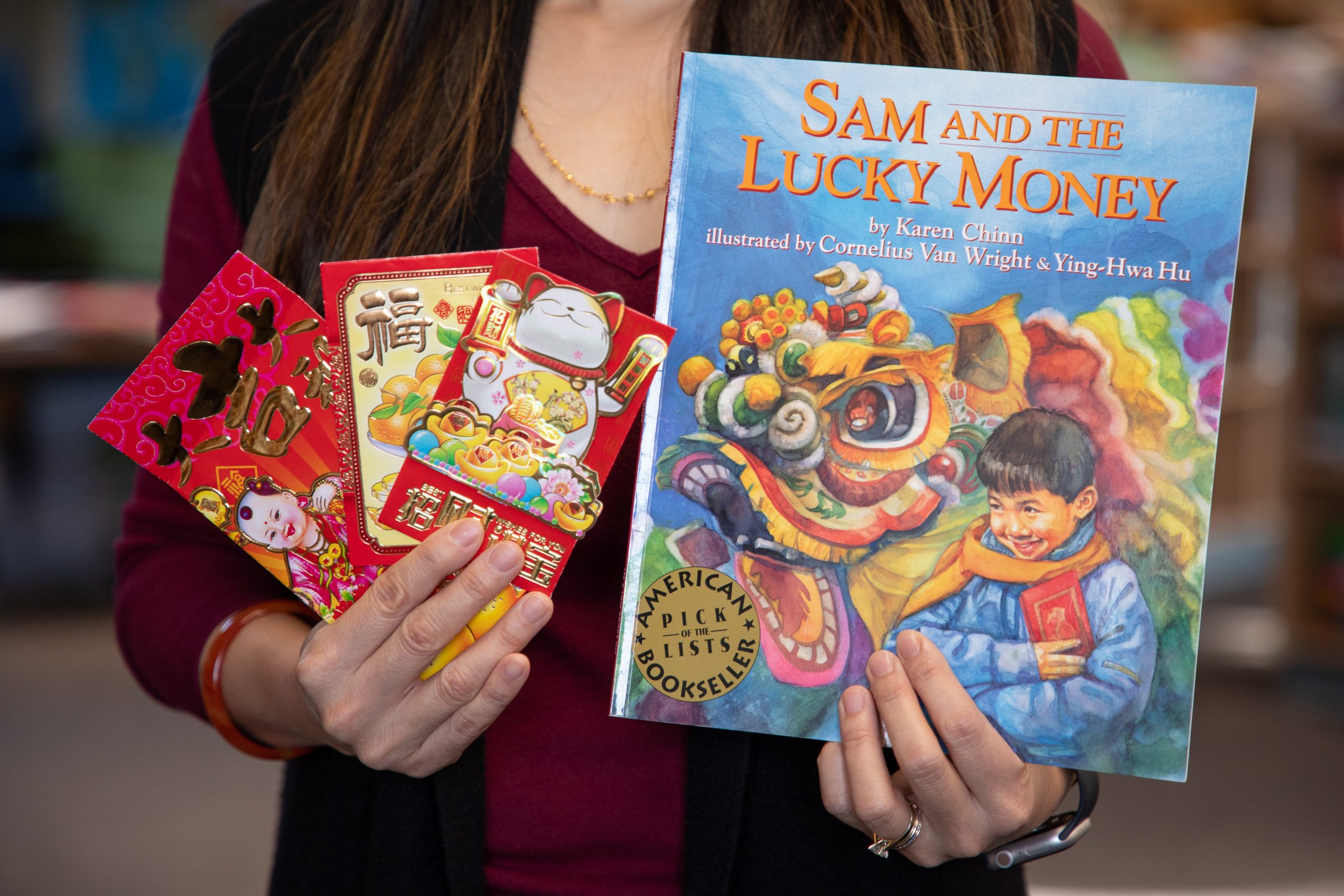 Cover of the book "Sam and the Lucky Money" by Karen Chinn along with three red envelopes for Lunar New Year.