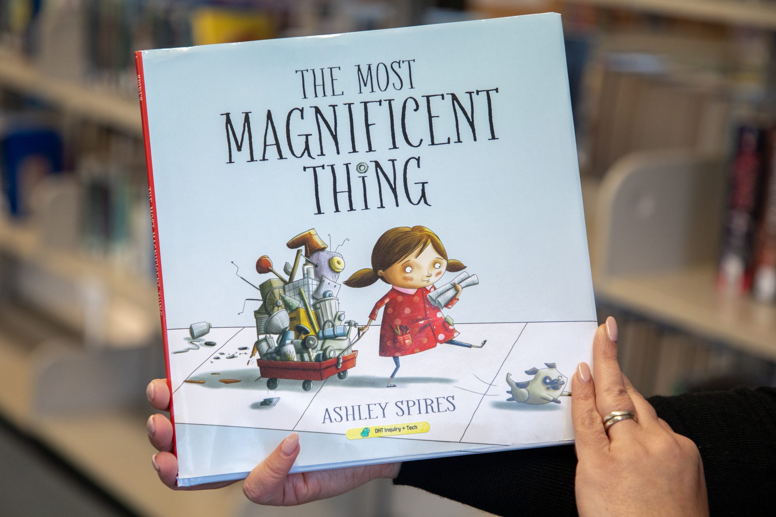 Book cover of "The Most Magnificent Thing" by Ashley Spires. A girl pulls a wagon holding various metal parts.
