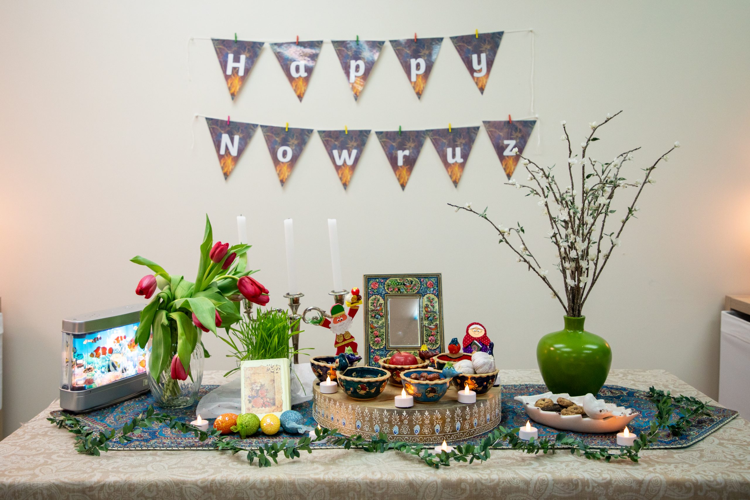 Haft-sin table with banner on the wall behind it that reads, "Happy Nowruz".